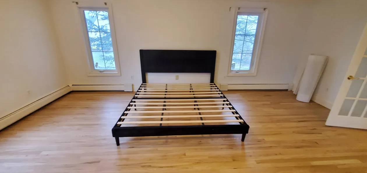 Dark bed frame with an upholstered headboard in a mostly empty room.